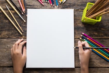 A child drawing on a sheet of blank white paper with coloured pencils