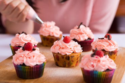 teenage girl decorating cupcakes with pink icing and raspberries