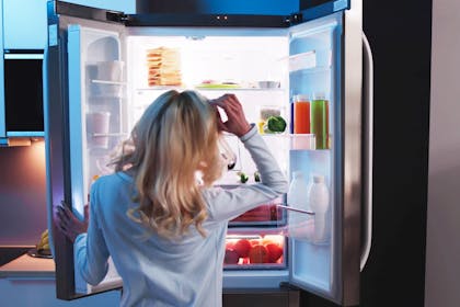 Pregnant woman standing at refrigerator deciding what to eat